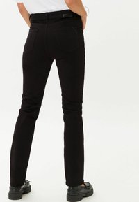 Schwarze Denim-Jeans mit schmaler Passform, ausgestattet mit Gesäßtaschen und leichtem Stretch. Kombiniert mit klobigen schwarzen Schuhen für einen Kontrast.