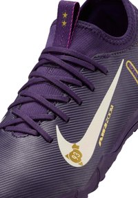 Scarpa da ginnastica viola con tomaia testurizzata, logo swoosh bianco, dettagli dorati e lacci viola. Presenta una linguetta in tessuto arrotondata.
