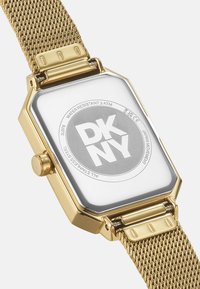 Orologio con cinturino in maglia d'oro, cassa rettangolare, quadrante bianco, logo "DKNY" bianco e nero e superficie texturizzata e lucida. Resistente all'acqua fino a 3 ATM.
