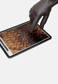 Rudos odinės pirštinės palietimas planšetės, ant kurios matomas tekstūruotas rudas paviršius su logotipu ir skaitmeninių sąsajos elementų b alta fonu.