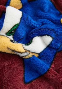 Fleece blanket featuring a vibrant blue and yellow character design on a maroon background, with soft, textured fabric.