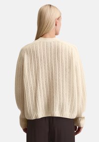 Cremefarbener Strickpullover mit vertikalem Streifenmuster, Lochdetails, gerippten Ärmelbündchen und lässiger Silhouette.