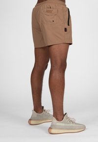 Bañador corto color marfil con cintura elástica, que cuenta con un bolsillo lateral con cremallera y un bolsillo trasero con cierre de botón. Combinado con zapatillas deportivas beige.