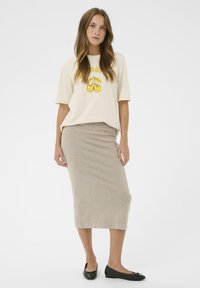Krémové tričko s žlutou grafikou třešní, doplněné těsně přiléhající béžovou midi sukní a černými balerínami. Hladká látka a jednoduchý design.