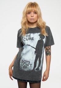Gray oversized t-shirt featuring a silhouette with a guitar, text "THE CURE" and "BOYS DON'T CRY," soft cotton material, distressed finish.