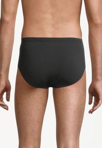 Slip da nuoto neri con un discreto motivo circolare, fascia elastica in vita e un tessuto liscio e morbido. Vista da dietro.