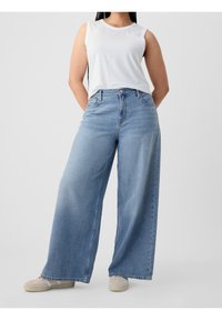 Jean large bleu clair à taille haute, en denim. Associé à un débardeur blanc avec un col rond.