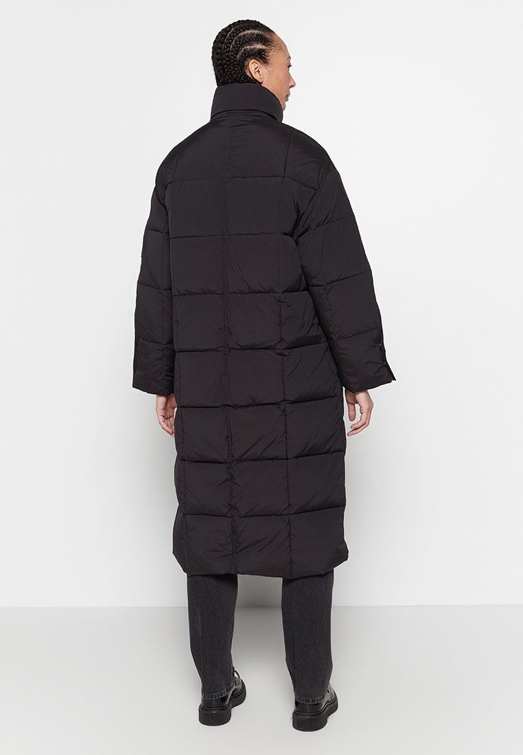 Schwarze Puffjacke mit einem langen, rechteckigen Design, breiten Bündchen und einem hohen Kragen. Verfügt über steppierte Abschnitte und eine glatte Textur.