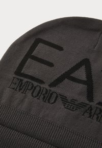 Sötétszürke sapka, amelyen fekete betűkkel feltűnően szerepel az "EA" betűsor és az "EMPORIO ARMANI" márkanev.