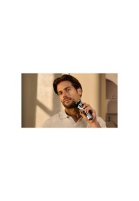 Rasoio elettrico ricaricabile con corpo argentato, design ergonomico e testa regolabile. L'utente lo tiene vicino ai peli del viso, indossando un polo chiaro.