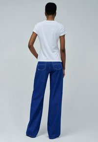 Camiseta blanca de manga corta y jeans amplios azules. La camiseta tiene un escote sencillo; los jeans cuentan con bolsillos traseros con costuras distintivas.