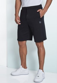 Schwarze Sportshorts mit elastischem Bund und Kordelzug, ausgestattet mit seitlichen Taschen und einem dezenten Logo am linken Bein.