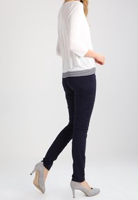 Weißes Oberteil mit einem schwarz-weiß gestreiften Saum, kombiniert mit navyblauen, taillierten Hosen und hellgrauen High-Heels. Glattes Material und taillierte Passform.