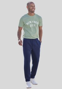Grünes Baumwoll-T-Shirt mit dem Aufdruck "NEW YORK CITY", kombiniert mit marineblauen Jogginghosen und weißen Sneakers. Lässiges Outfit, geeignet für den Alltag.
