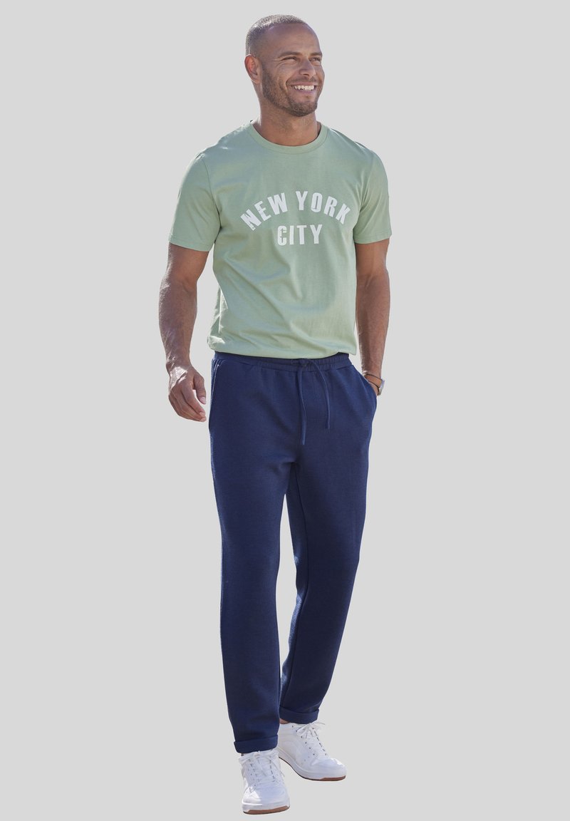 Grünes Baumwoll-T-Shirt mit dem Aufdruck "NEW YORK CITY", kombiniert mit marineblauen Jogginghosen und weißen Sneakers. Lässiges Outfit, geeignet für den Alltag.