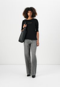 Black long-sleeve shirt with "TOM TAILOR" logo, paired with high-waisted gray wide-leg jeans and a black tote bag. Plain background.
