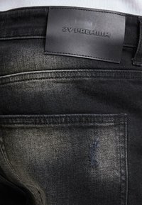 Czarne dżinsy z denimu z skórzaną etykietą w pasie, lekko wyblakłe oraz z przetartą łatą na tylnej kieszeni.