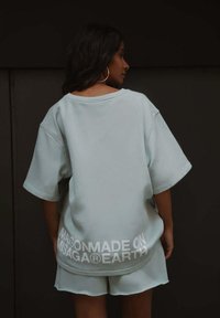 Lichtblauwe oversized sweatshirt gemaakt van zachte stof, met korte mouwen en een witte logo detail aan de onderkant. Gecombineerd met bijpassende shorts.