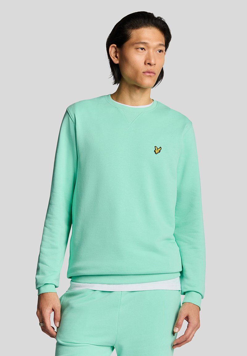 Sudadera verde menta de material suave con cuello redondo y mangas largas. Incluye un pequeño logotipo amarillo en el pecho.