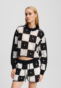 Ingekorte zwart-witte geblokte trui met kantpatroon, gecombineerd met bijpassende shorts met een elastische tailleband en trekkoord.