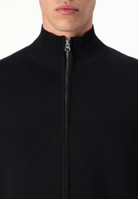 Black knit zip-up sweater featuring a high collar, ribbed texture, and metal zip closure down the front. Minimal design without patterns.