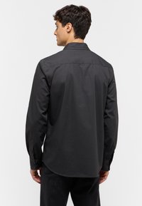 Camisa negra de manga larga con collar, textura suave y puños abotonados. La parte trasera presenta un yugo y un diseño de dobladillo redondeado.
