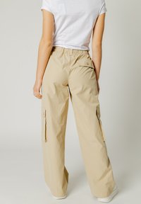 Pantaloni cargo beige con vestibilità rilassata, vita elasticizzata, tasche laterali e dettagli di cucitura sottili. Il materiale sembra leggero e liscio.