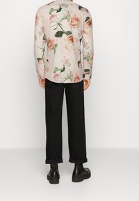 Camicia a maniche lunghe con motivo floreale che presenta colori rosa chiaro, crema e verde, abbinata a pantaloni neri con risvolto e scarpe nere chunky.