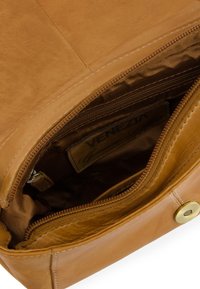 Tan leather handbag interior featuring a zippered pocket, smooth texture, gold-tone hardware, and a fabric lining with logo.