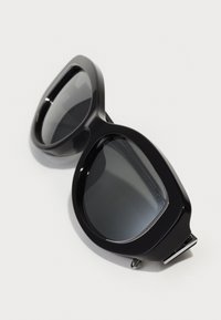 Black sunglasses with a thick, glossy frame, gray lenses, and a silver accent near the hinge. Rounded shape with wide coverage.