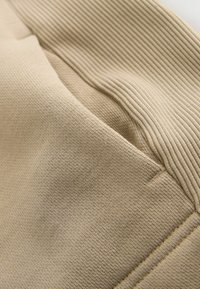 Detailný záber na béžové rebrované a hladké úpletové časti so zreteľným prešívaním švov.