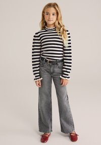 Un top cu dungi negre și albe, cu mâneci lungi și guler volănit, asortat cu blugi gri cu talie înaltă și pantaloni largi, purtați cu pantofi roșii fără toc.