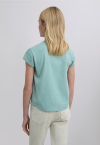 Haut bleu clair à manches courtes avec un col arrondi et une coupe décontractée. Associé à un pantalon de couleur crème. Matière en coton doux, texture lisse.