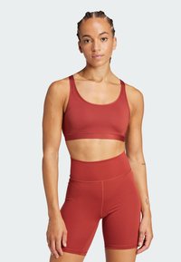 Sujetador deportivo rojo y pantalones cortos de cintura alta, hechos de una tela elástica. Textura suave con costuras en contraste y un diseño minimalista.