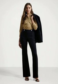 Tan button-up shirt, high-waisted black pants with stripes, and a black blazer draped over the arm. Black heels complete the outfit.