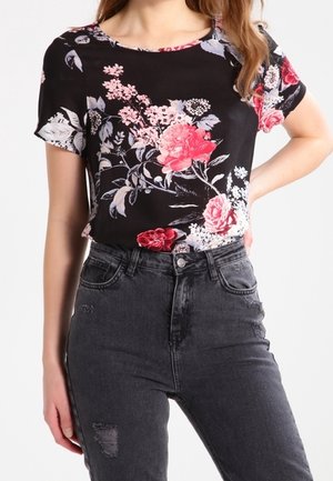 Mujer con blusa negra de flores de manga corta metida en vaqueros negros descoloridos de cintura alta con ligeros desgastes.