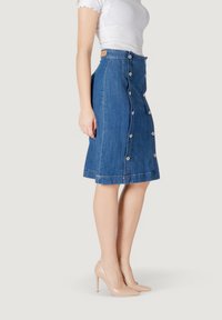 Falda de mezclilla en azul medio con corte recto, presenta botones en el frente y un dobladillo justo por encima de la rodilla. Textura suave y diseño clásico.