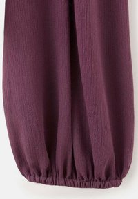 Bordowy, fakturowany materiał z marszczoną gumką u dołu, tworzący miękki i drapowany kształt. Lekki i zwiewny fason.