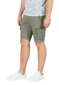 Green cargo shorts with rolled cuffs, side pockets, and a textured finish. Paired with white sneakers and a patterned shirt.