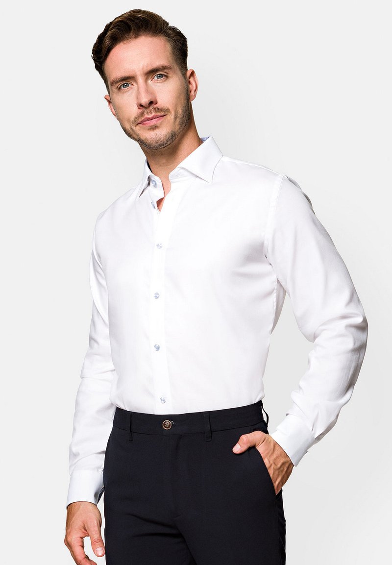 Biała, długosleeve koszula z guzikowym kołnierzykiem i jasnoniebieskimi guzikami. Gładki materiał, dopasowany krój, noszona z ciemnymi spodniami.