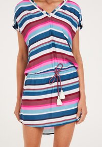 Robe rayée avec un décolleté en V, des manches courtes et un cordon de taille ajustable. Les couleurs incluent le bleu, le rose, le blanc et le marron. Comprend des pompons.