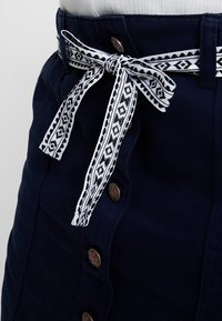 Navy blue skirt with a textured finish, featuring a patterned black and white belt, and brown button accents along the front.