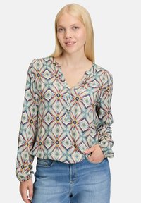 Long-sleeve blouse in a light fabric featuring a geometric pattern in teal, pink, and yellow. Notched collar with button details and gathered sleeves.