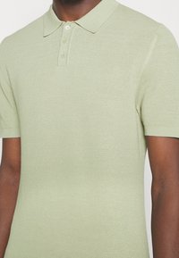 Sweterkowa koszulka polo w jasnej zieleni z teksturowanym wzorem, krótkimi rękawami i dwukolorową plisą z dwoma guzikami. Miękka, lekka tkanina.