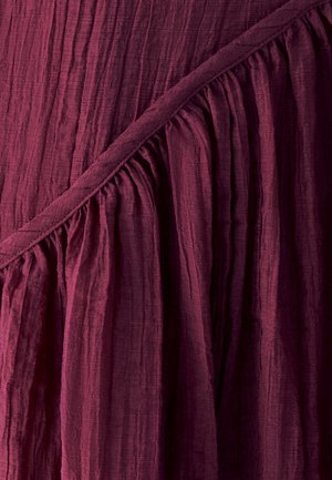 Bordeaux stof met een gekreukt textuur en geplooide details, met een diagonaal stiksel langs de rand, wat een gelaagde visuele interesse creëert.