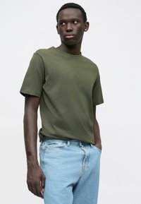 Olivově zelené bavlněné tričko s kulatým výstřihem, krátkými rukávy a volným střihem. Kombinováno s džínami v světle modré barvě. Minimalistický design.