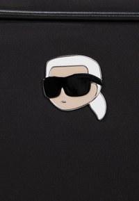 Black textured fabric featuring a metal emblem of a face with sunglasses, light skin tone, white hair, and silver accents.