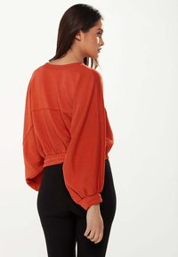 Orange cropped sweatshirt with balloon sleeves, ribbed waistband, and textured fabric, paired with black ribbed high-waist pants.