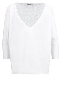 Pull blanc ample en maille avec col en V, manches chauve-souris longues et une étiquette Calvin Klein Jeans à l'intérieur du col.