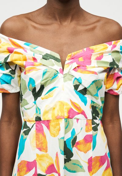 Tumšādains cilvēks, kurš valkā krāsainu, no pleciem nokareno kleitu ar uzpūstām piedurknēm un ziedu rakstu dzeltenā, rozā, zilā un zaļā krāsā.